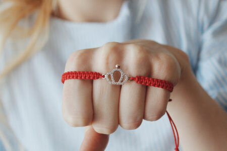 closeup shot red thread bracelet with silver crown pendant female s hand